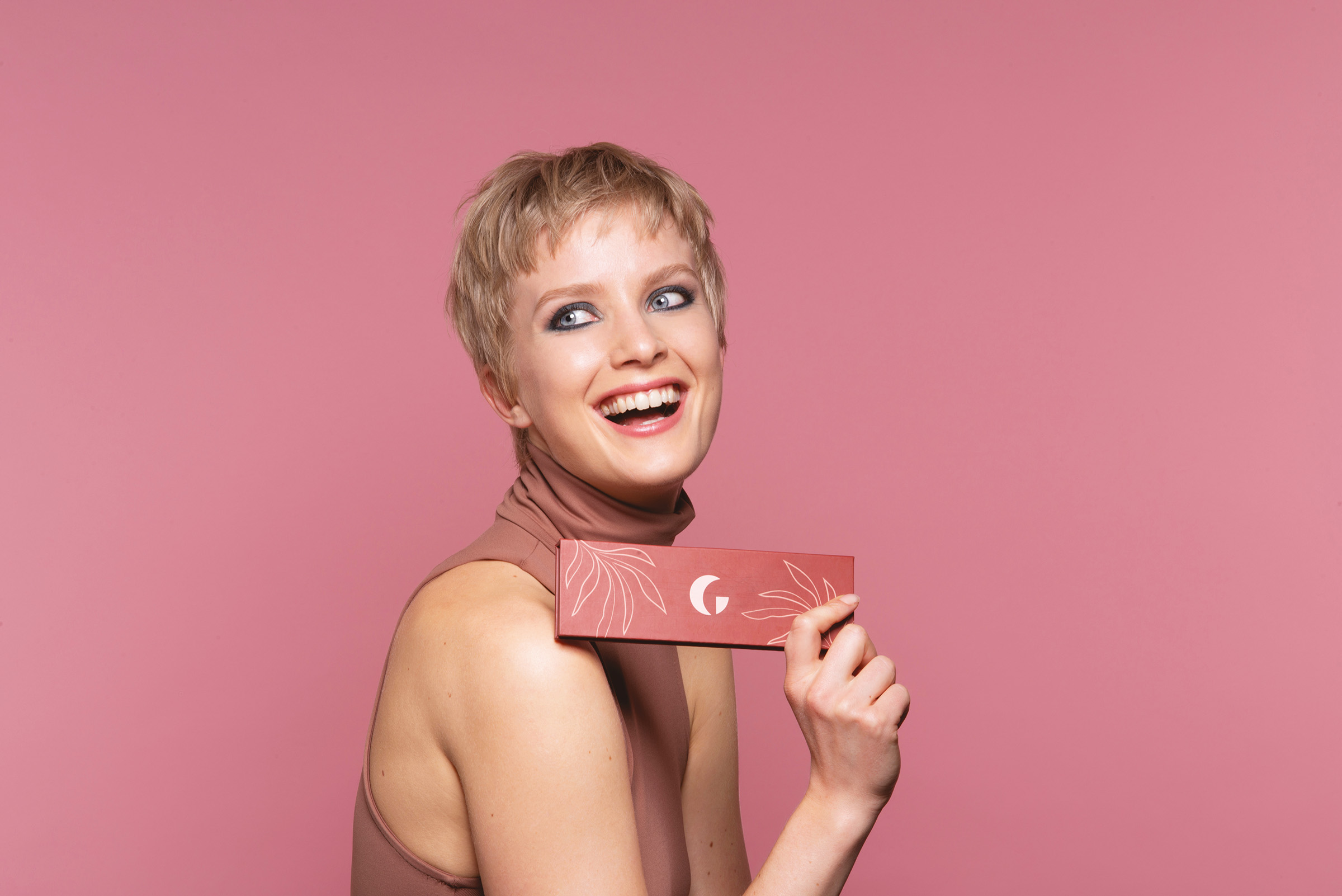 Woman on a pink background holding a Gabriella's eyeshadow palette